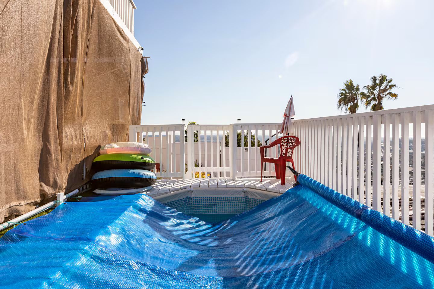 A pool with a blue inflatable slide, a white fence, and a red chair.
