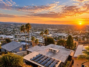 Una azotea con paneles solares, rodeada de edificios residenciales y palmeras, al atardecer.