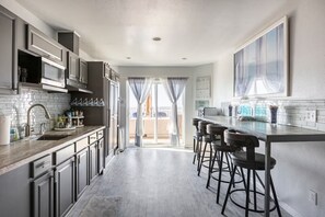 A modern kitchen with a central island, bar stools, and a view to the outside.