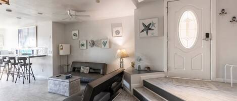 A modern living room with a sofa, a coffee table, and a dining area with bar stools.
