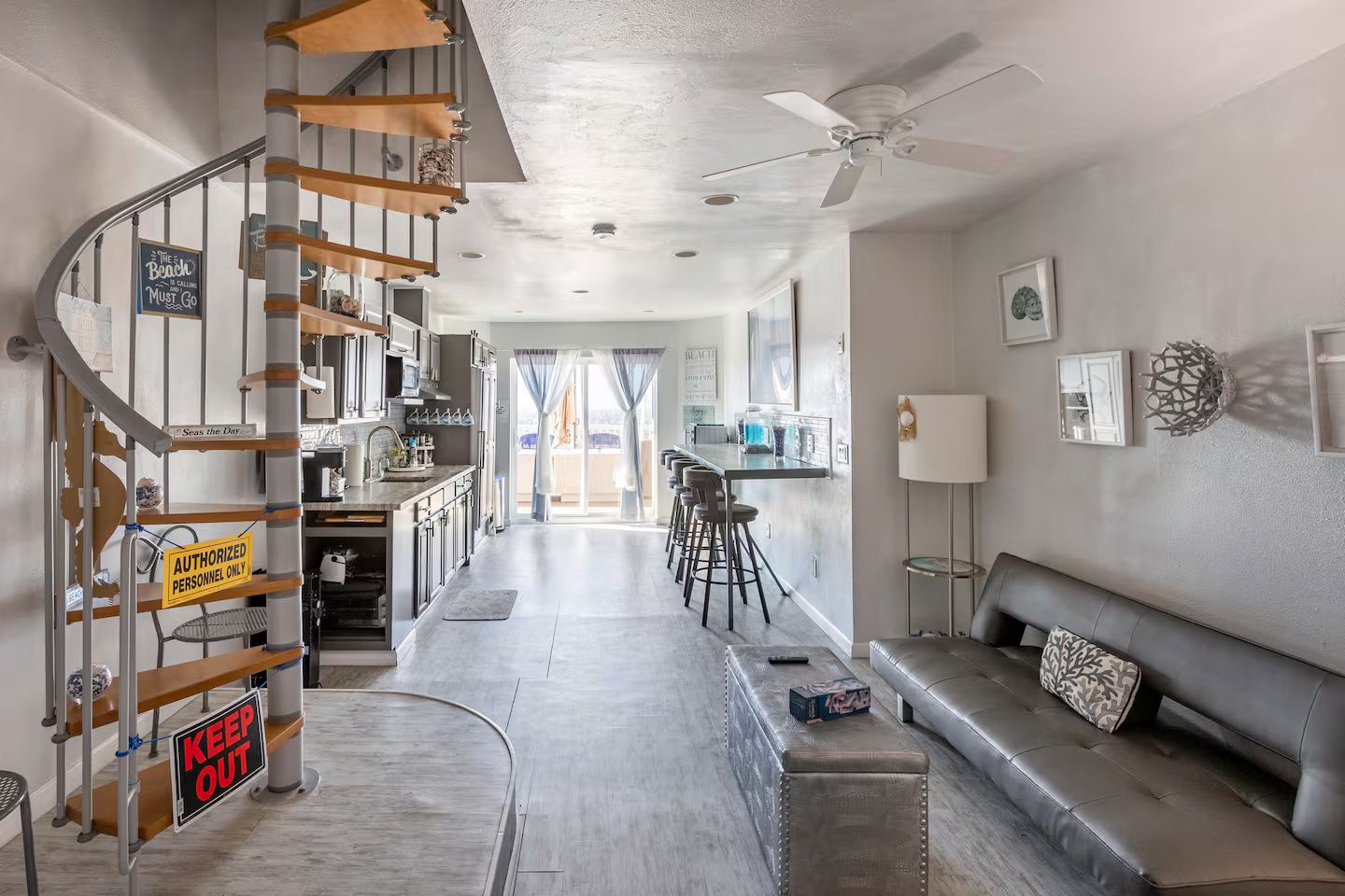 A modern interior with a staircase, kitchen, dining area, and a seating area with a sofa and ottoman.