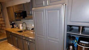 A kitchen with grey cabinets, a stainless steel refrigerator, a microwave, and a blender on the counter. - Beach Vibes (Spring Valley)
