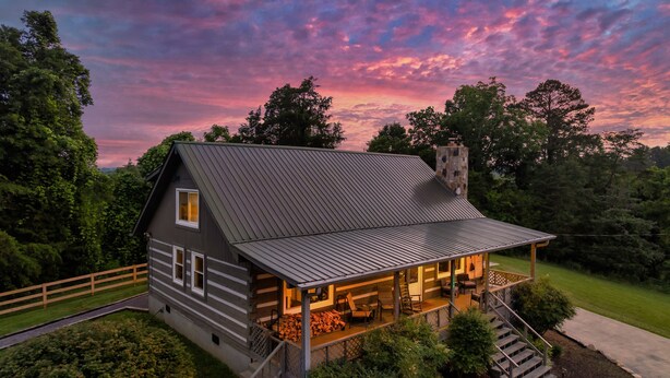 A log cabin with a porch, a chimney, and a view of the surrounding forest.
