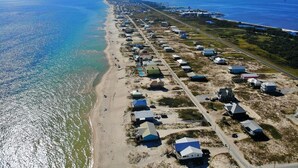 Vista aérea de una zona costera con una hilera de casas de playa a lo largo de la orilla, una carretera y un barco distante en el agua.