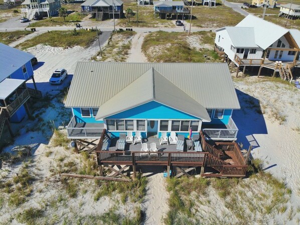 A beachfront house with a large deck, multiple balconies, and a swimming pool.