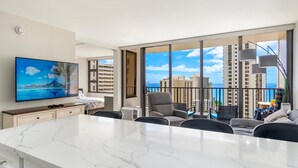 A modern hotel room with a large TV, a marble dining table, and a balcony with a city view. - Luxurious, Free Parking & WiFi, Ocean View, Remodeled, 1 Bed Room, No Resort Fee (Honolulu)