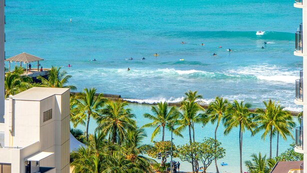 A coastal view with palm trees, a beach, and a building with a pool. - Luxurious, Free Parking & WiFi, Ocean View, Remodeled, 1 Bed Room, No Resort Fee (Honolulu)