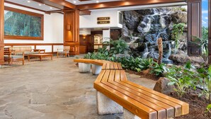 A lobby with a stone floor, wooden benches, a waterfall feature, and a sign indicating 'TOWER MAKAI'. - Luxurious, Free Parking & WiFi, Ocean View, Remodeled, 1 Bed Room, No Resort Fee (Honolulu)