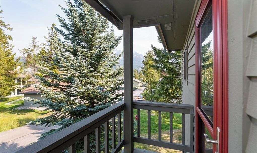 A balcony with a view of a coniferous tree and a residential area.