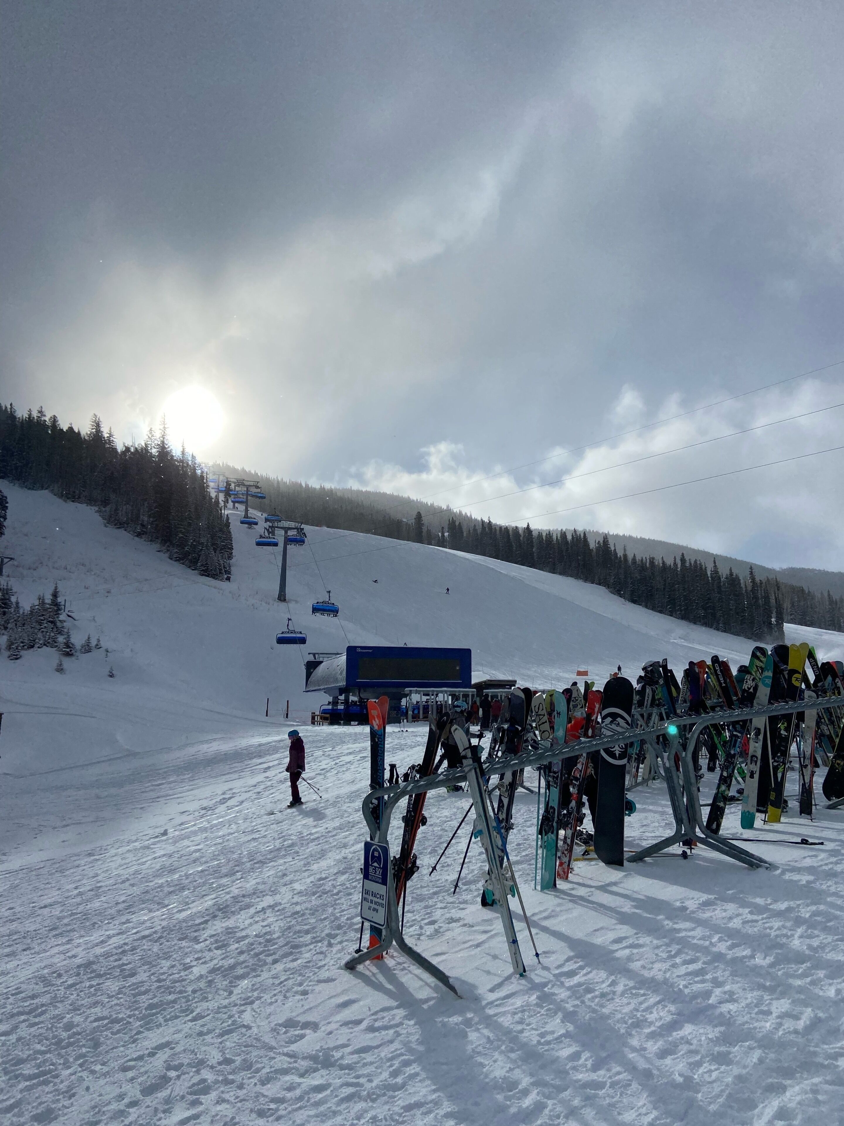 A ski slope with a ski lift, a row of skis, and a sign indicating no backcountry skiing.