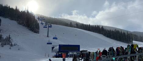 A ski slope with a ski lift, a row of skis, and a sign indicating no backcountry skiing.