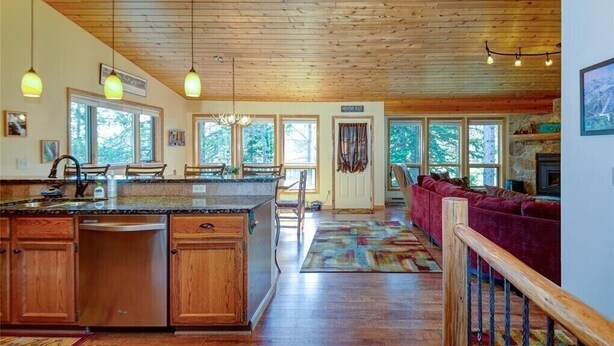 A spacious kitchen with wooden cabinets, a granite countertop, and a large island. There is a dining area with a red sofa and a fireplace.