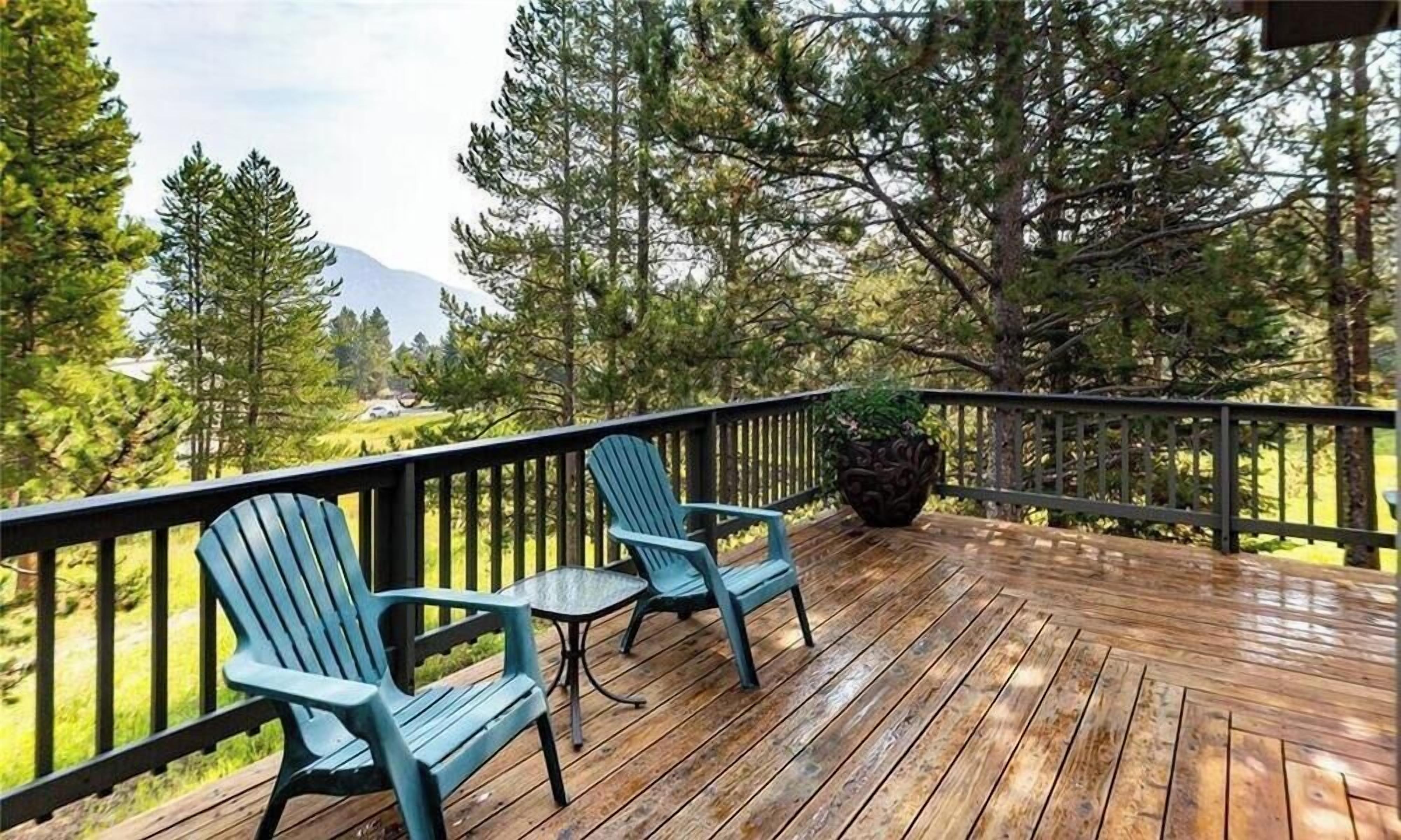 Eine Holzterrasse mit zwei Adirondack-Stühlen und einem Blumentopf.
