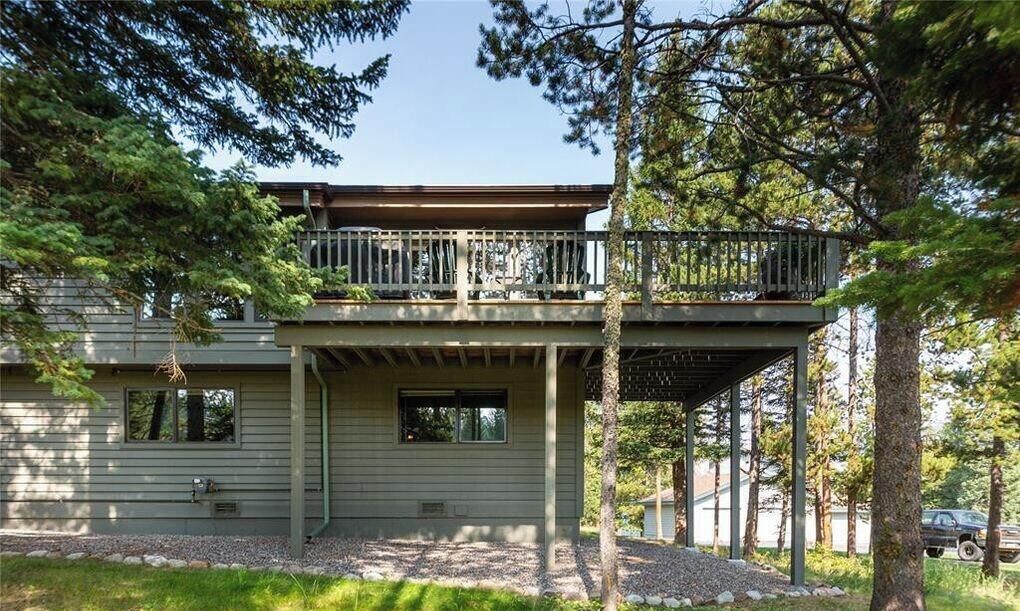 Une maison à deux étages avec un balcon, entourée d’arbres et donnant sur une allée gravillonnée.