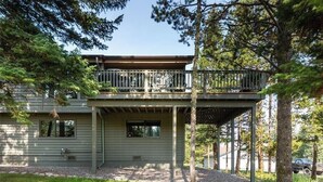 A two-story house with a balcony, surrounded by trees and a gravel driveway.