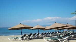 Une plage bordée de rangées de transats et de parasols, un ciel dégagé et l’océan en toile de fond.