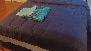 A bedroom with a wooden bed, a dark blue bedspread, and a green blanket.