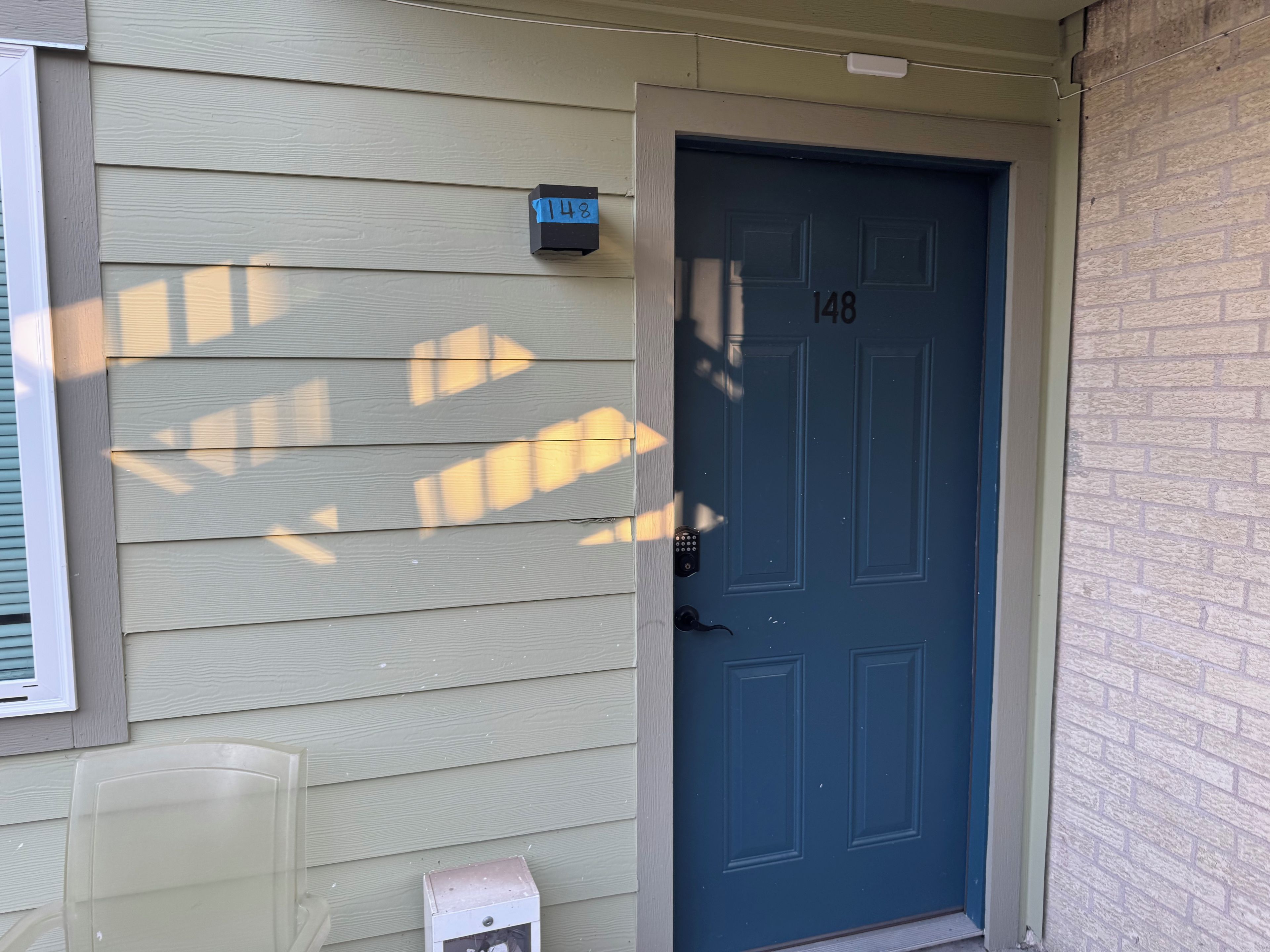 A blue door with the number 148, a mailbox, and a clear plastic chair.