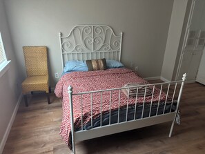 Een slaapkamer met een bed met metalen frame, een beddengoed met een patroon, een stoel en een kledingkast.