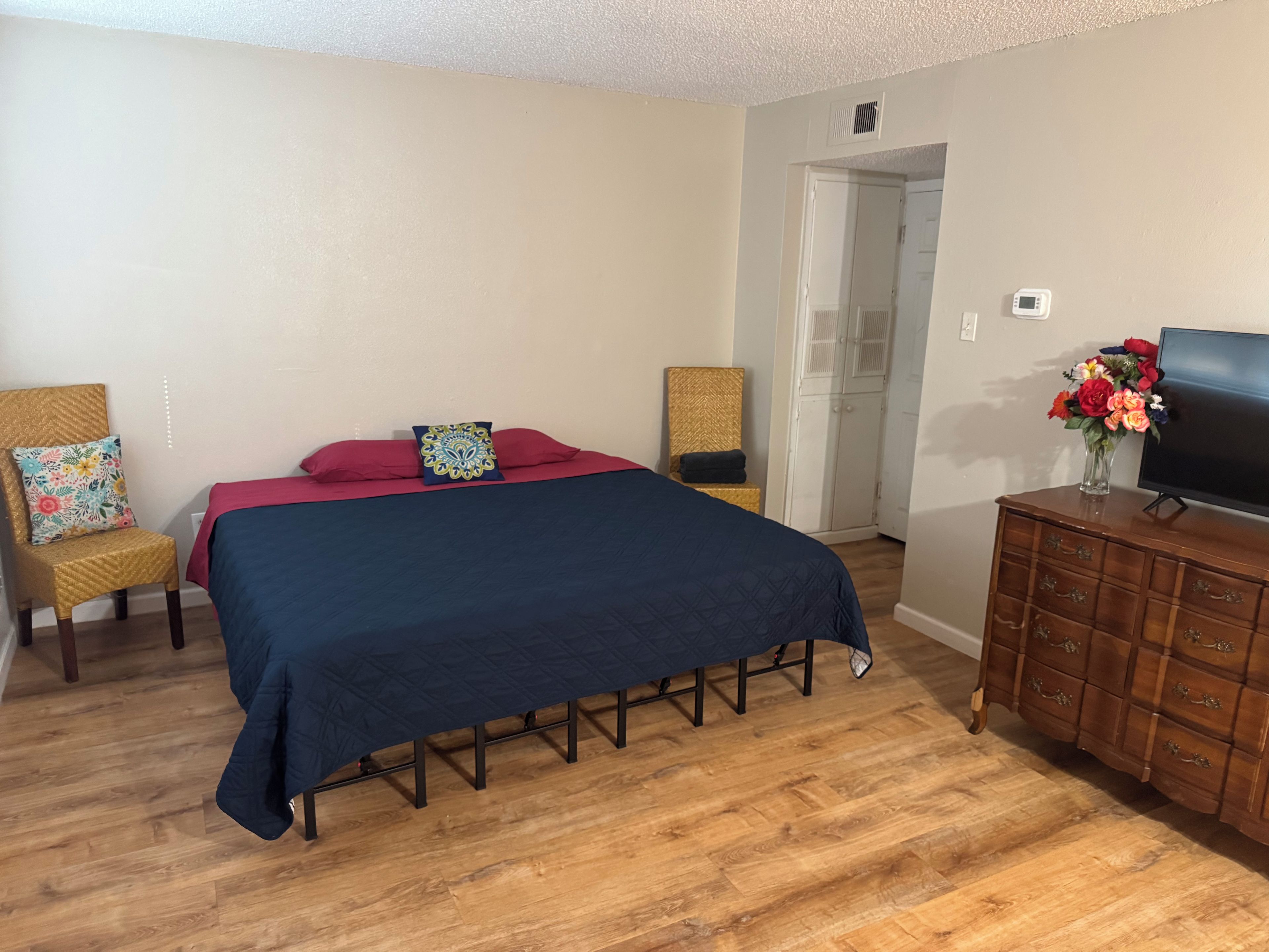 Un dormitorio con una cama, un aparador, un televisor y una puerta que da a otra habitación.