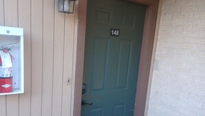 A green door with the number 148, a fire extinguisher mounted on the wall, and a green mat at the entrance.