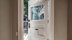 Eine weiße Tür mit Glasfenster, eine Holzterrasse und ein Stuhl mit gestreifter Sitzkissen.