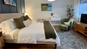 Ein Schlafzimmer mit Bett, Nachttisch, Sessel, Fernseher und Kunstwerken an den Wänden.