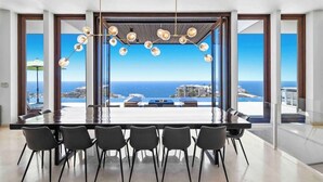 Een moderne eetruimte met een grote tafel en stoelen, grote ramen met uitzicht op de oceaan, en een bijzondere kroonluchter.