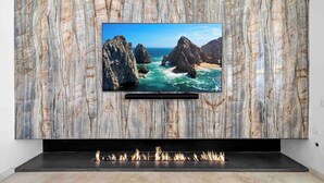 Een flatscreen televisie bevestigd aan een marmeren muur met een open haard eronder.