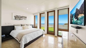 Een slaapkamer met een bed, een televisie en een groot raam met uitzicht op de oceaan.