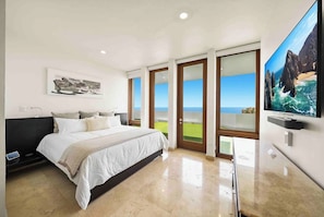 Een slaapkamer met een bed, een televisie en een groot raam met uitzicht op de oceaan.