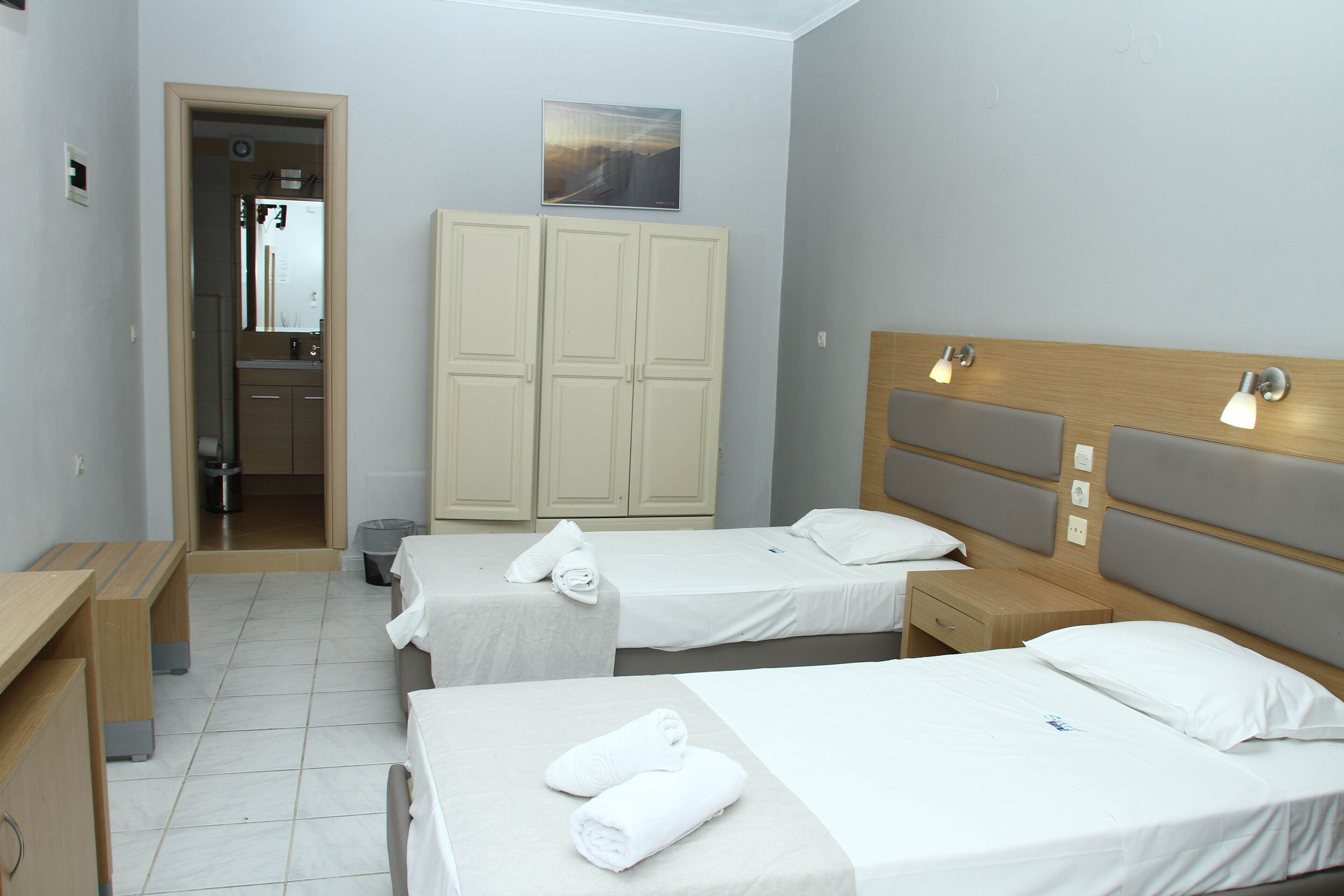 Habitación de hotel con dos camas individuales, cabecera de madera, un escritorio pequeño, un espejo y un armario.