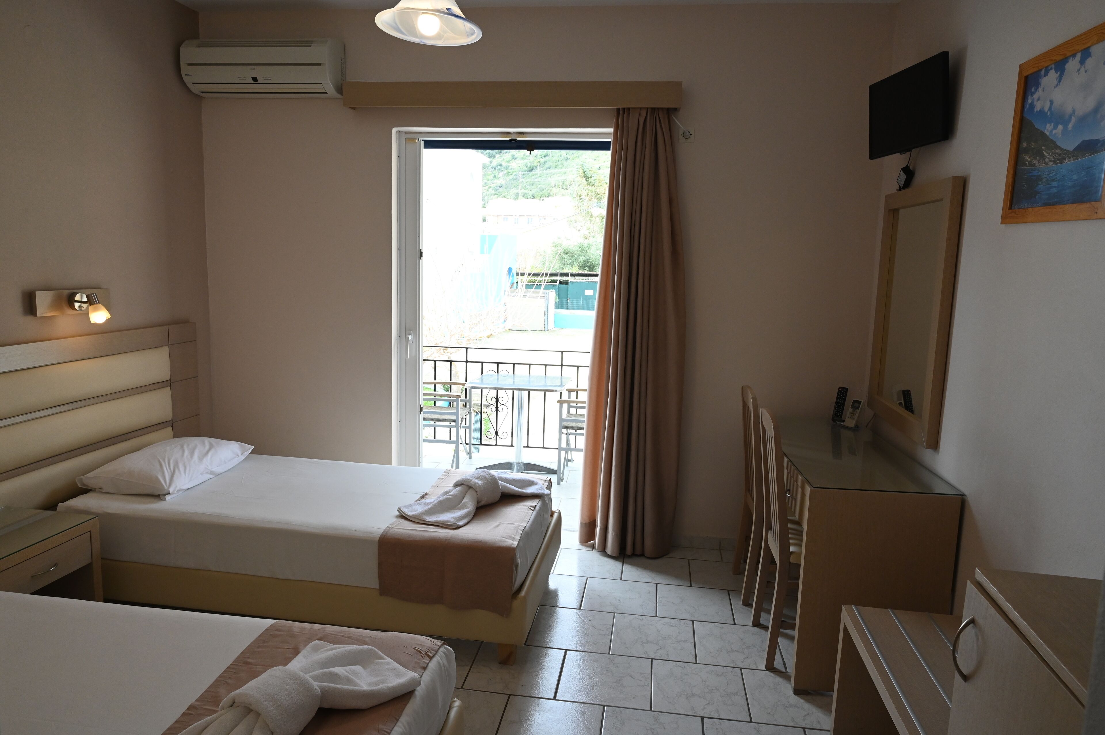 A hotel room with two beds, a TV, a mirror, and a balcony with a view of the outside.