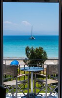 Un balcón con sillas de mimbre y una mesa, con vista a una playa de aguas azules cristalinas y un velero.