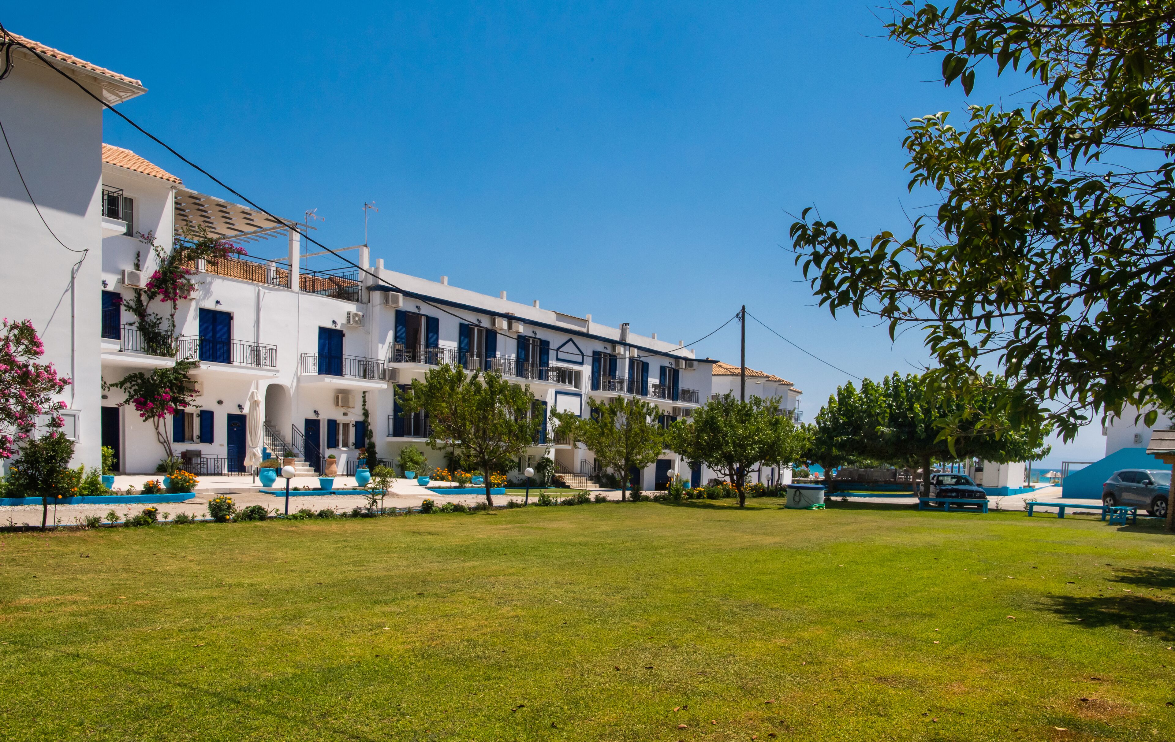 A row of white buildings with blue accents, a grassy courtyard, and trees.