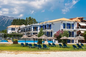 Un hotel frente a la playa con varios balcones, zona de piscina y sillones de descanso.