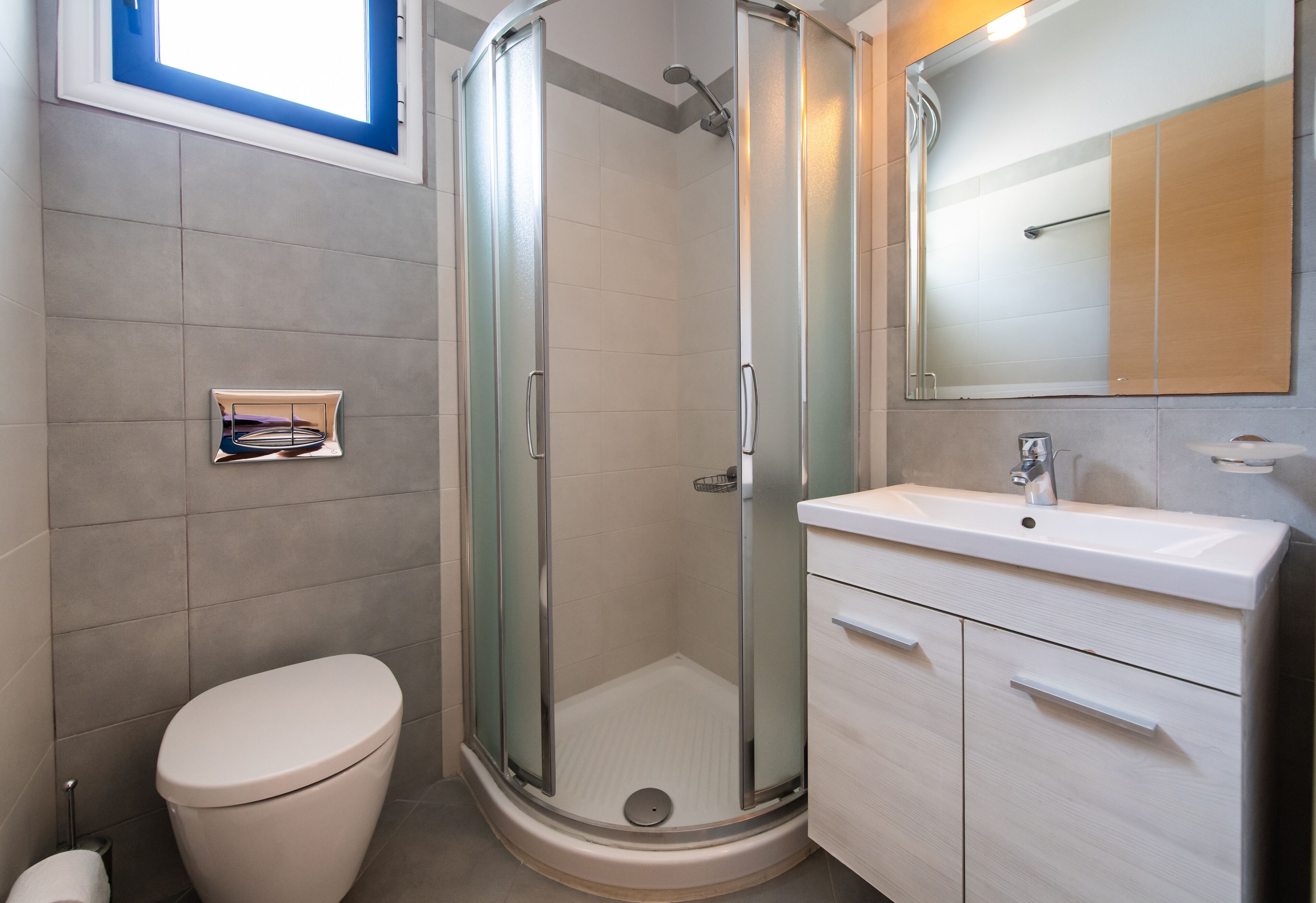 Un baño moderno con ducha de vidrio, inodoro, lavabo y espejo.
