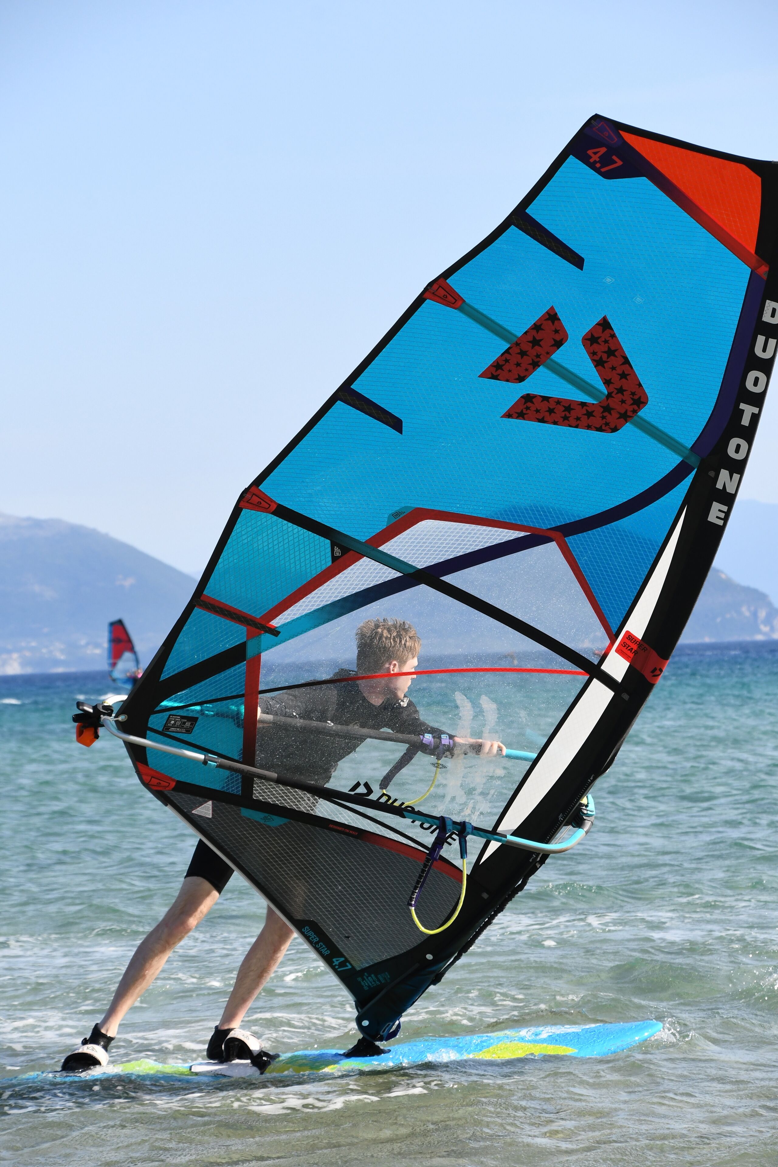 A person windsurfing on a clear day with calm waters and distant mountains.
