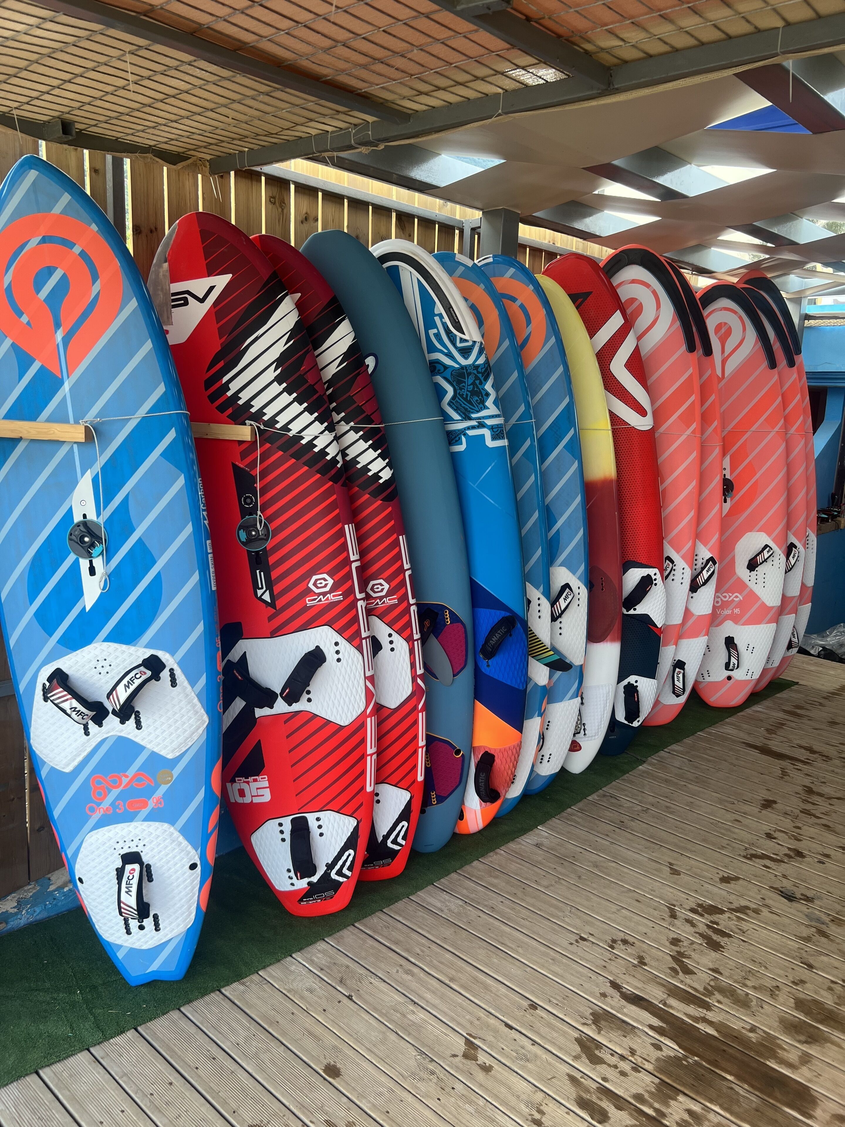 A row of snowboards with various designs and colors, displayed indoors with a wooden floor and a metal ceiling.