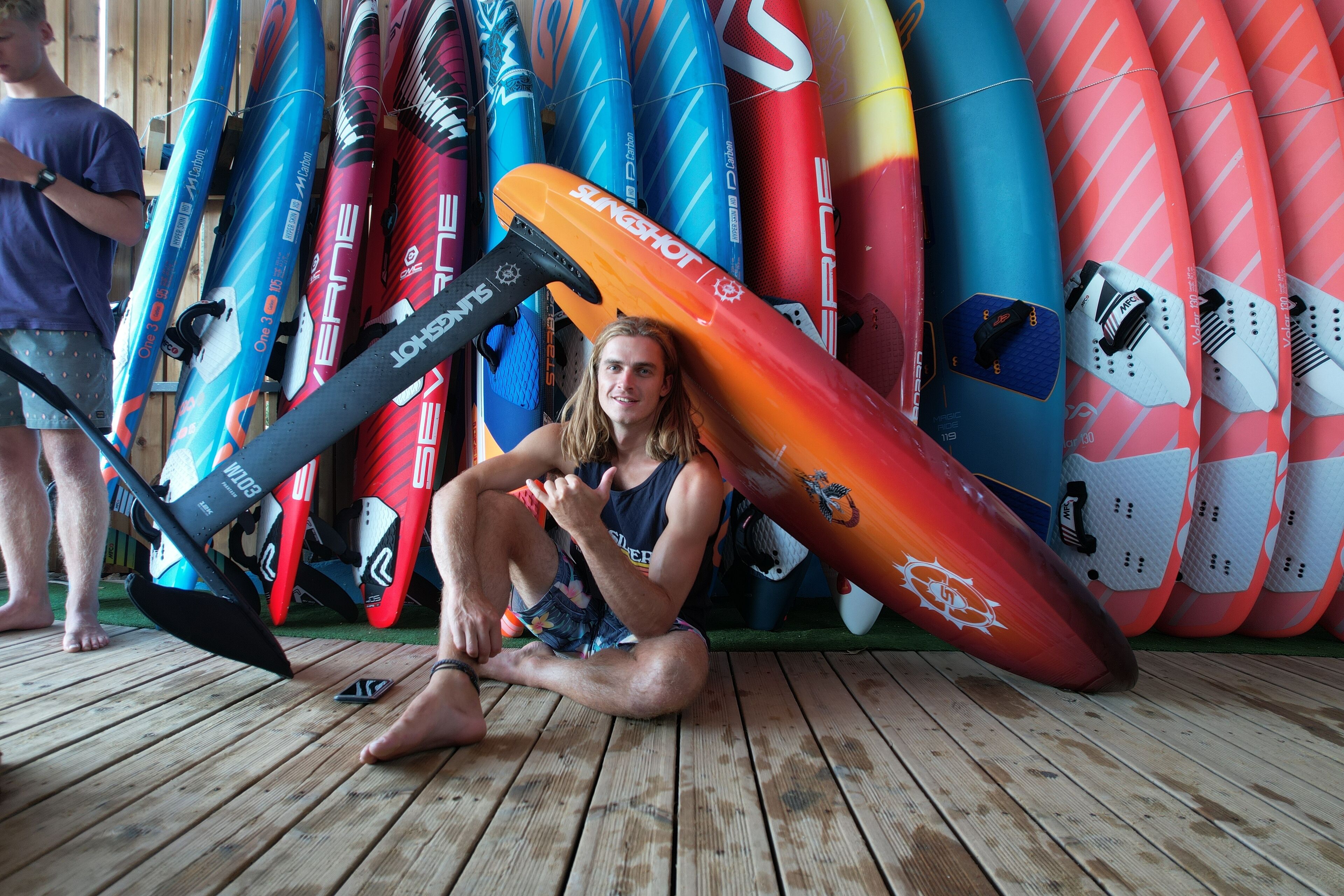 A person sitting on a wooden deck surrounded by various surfboards.