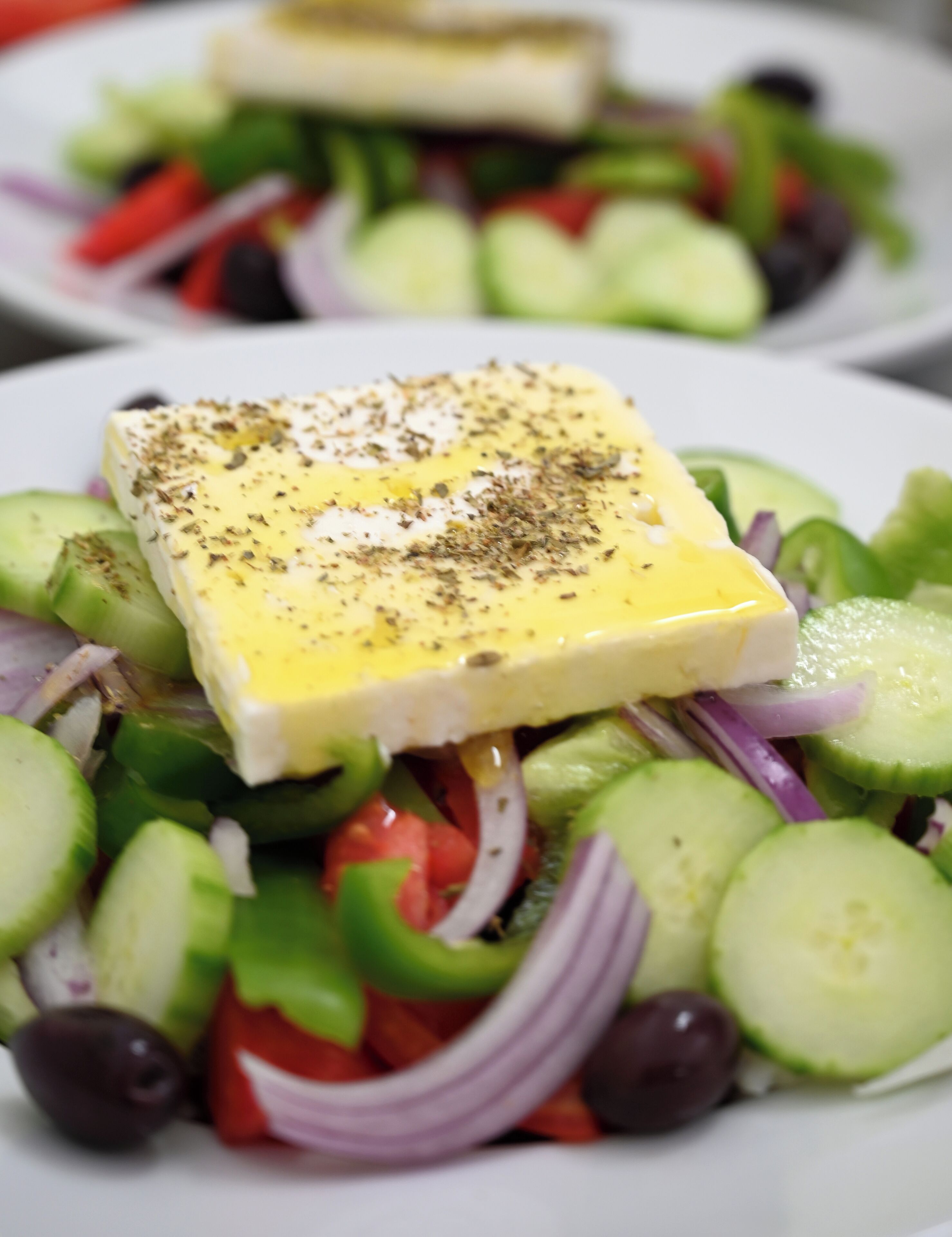 A plate of Greek salad with feta cheese, cucumbers, tomatoes, red onions, and olives.