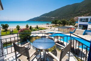 Un balcón con mesa y sillas que da a una playa y una zona de piscina.
