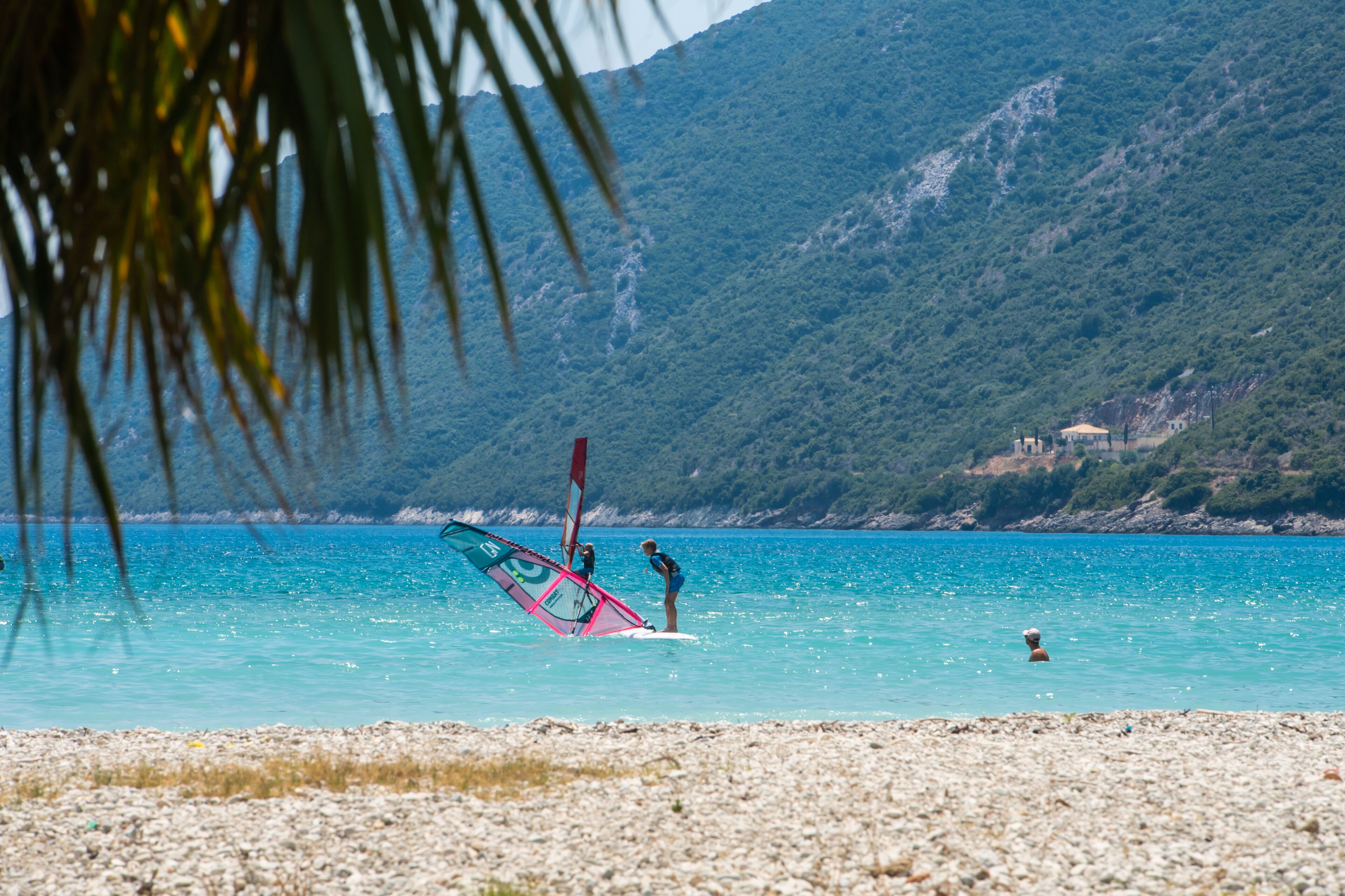 A beach with a rocky shoreline, a person windsurfing, and a mountain in the background.
