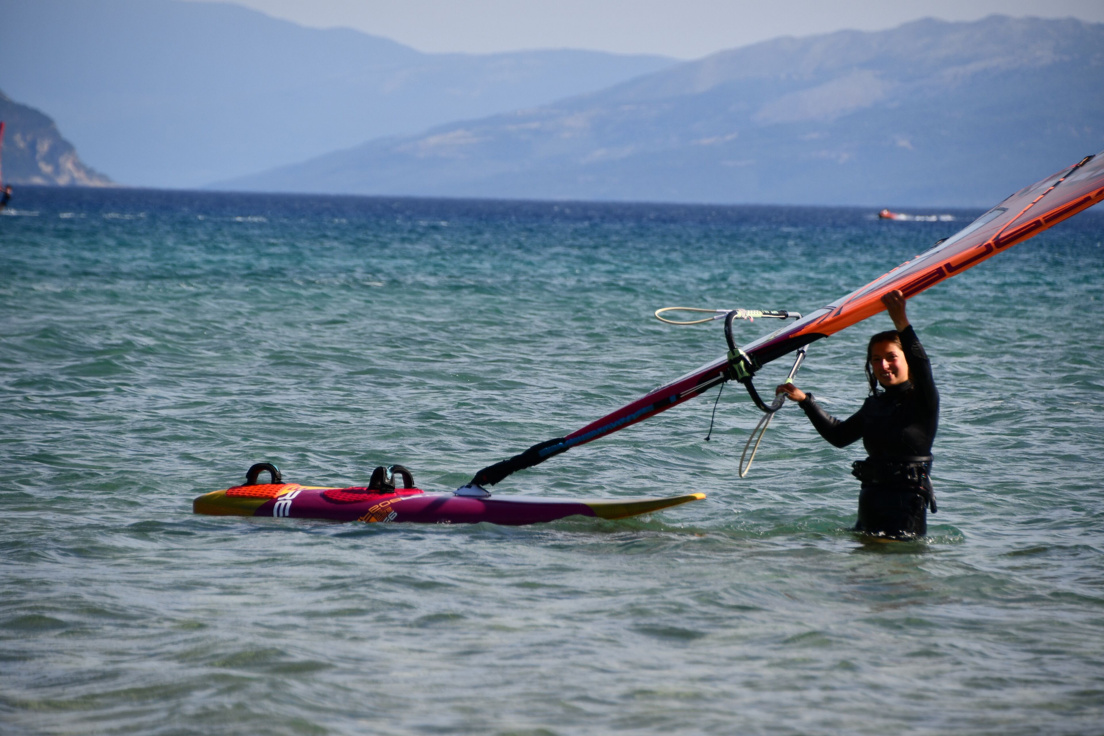 Una persona dret/dada en l'aigua aguantant una taula de windsurf.