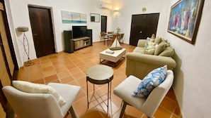 A living room with a sofa, chairs, a coffee table, a TV, and a dining area with chairs and a table. - Beautiful Villa with Golf Course, Ocean, and Rainforest Views. (Rio Grande)