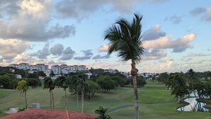 A golf course with a clubhouse, palm trees, and a residential area in the background. - Beautiful Villa with Golf Course, Ocean, and Rainforest Views. (Rio Grande)