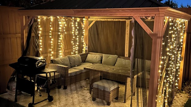 A covered patio area with a wooden bench, a grill, and string lights. - Close to everything and quiet for peace (Euless)