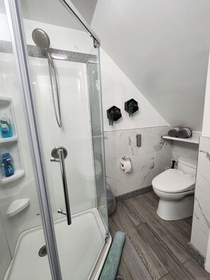 Un baño moderno con ducha envuelta en vidrio, inodoro y suelo de mármol.