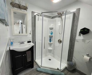 Un baño moderno con ducha envuelta en vidrio, un lavamanos blanco y un espejo encima.