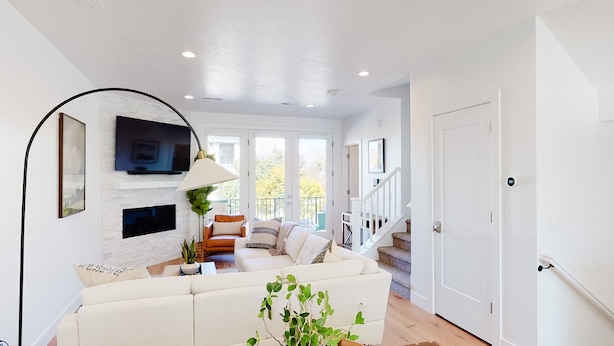 A spacious living room with a white sofa, a TV mounted on the wall, and a staircase leading to an upper floor.